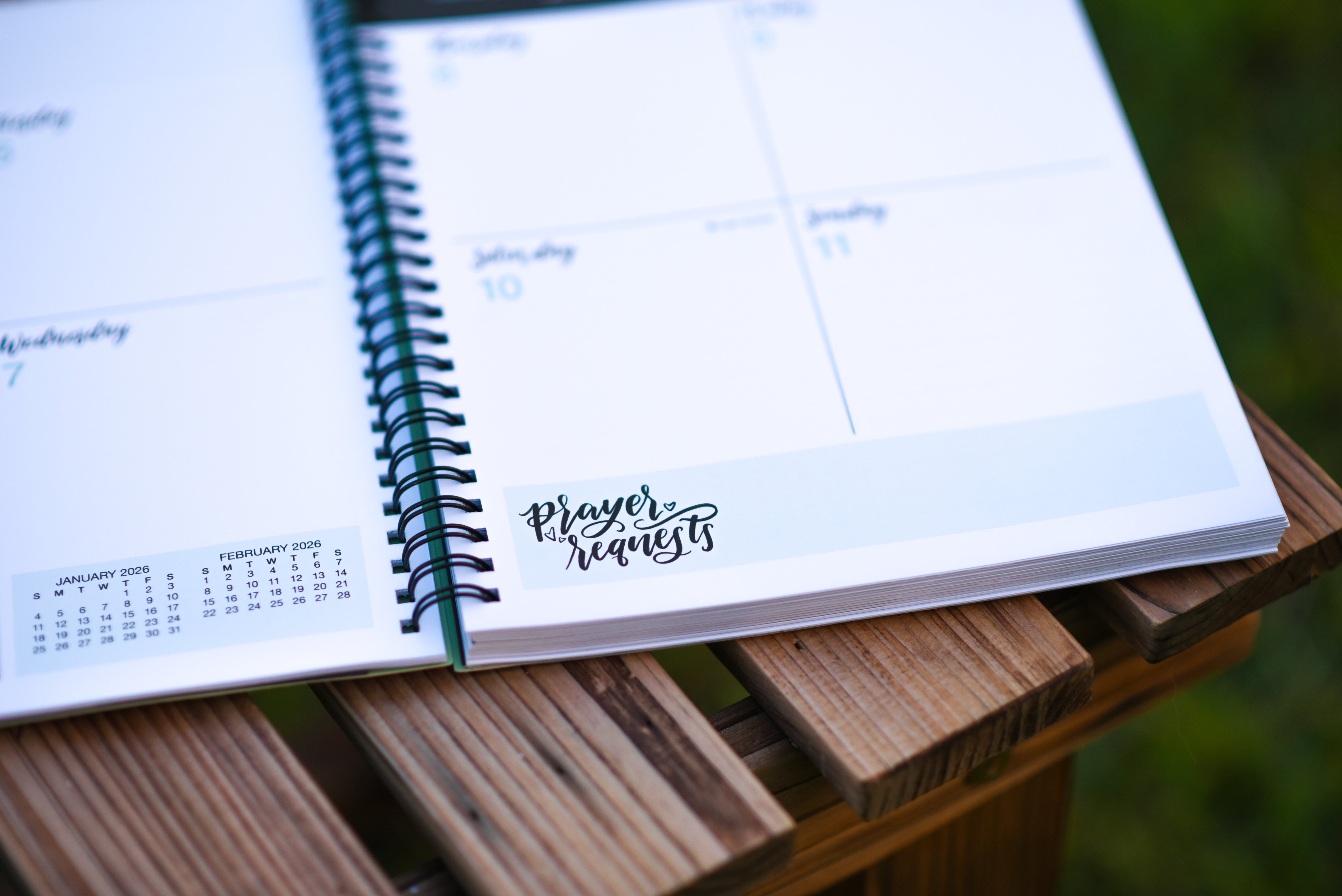 Open planner with prayer requests on a wooden surface outdoors