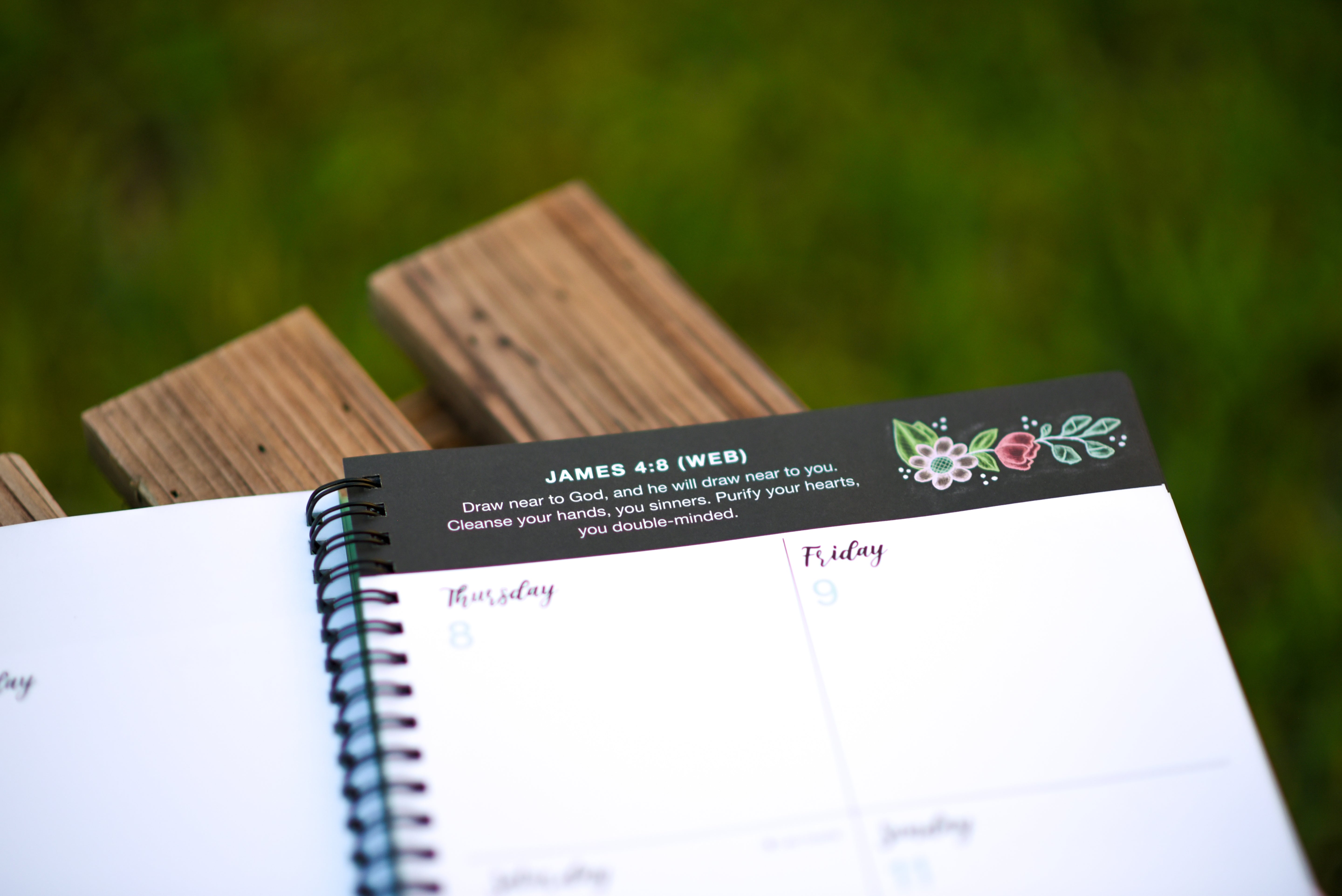 Notebook with a decorative border featuring a Bible verse scripture and illustrations on a wooden surface.