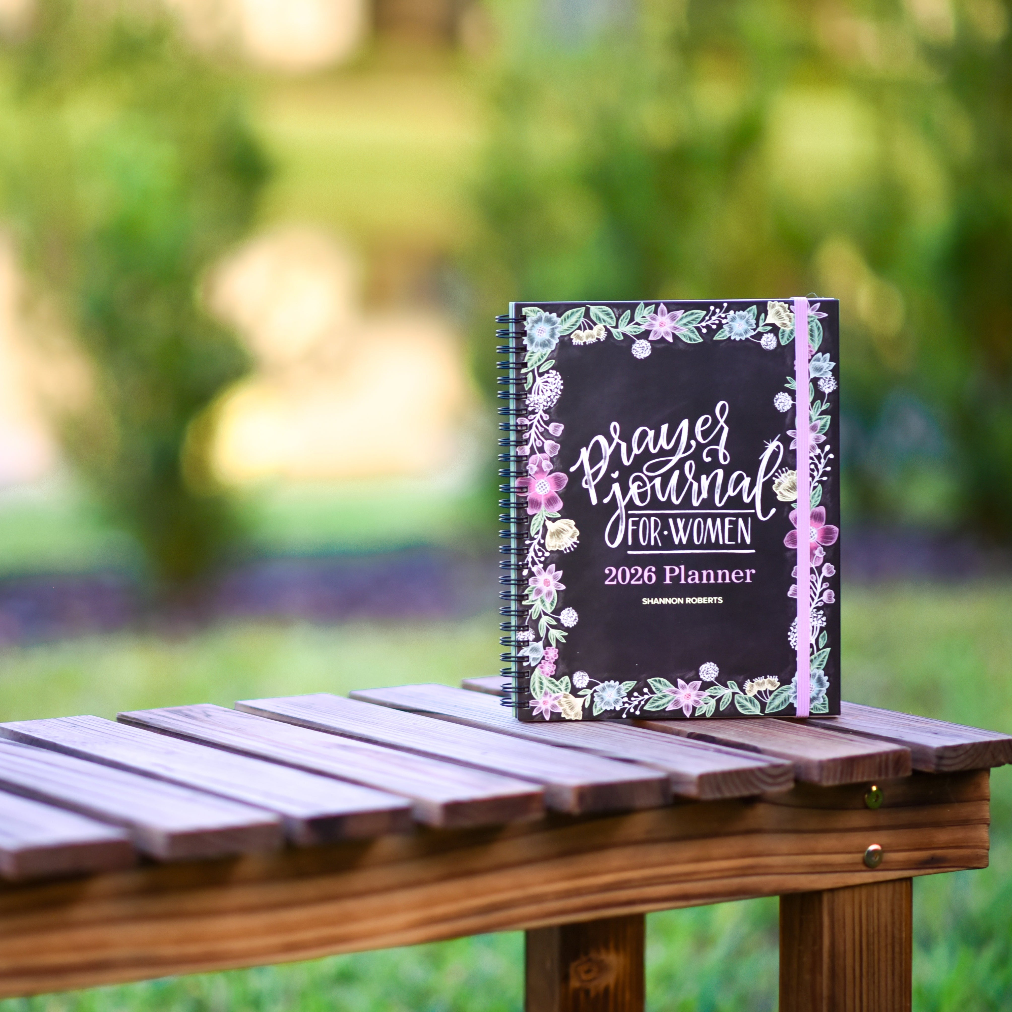 Planner titled 'Prayers & Journal for Women 2026 Planner' on a wooden table with a blurred natural background