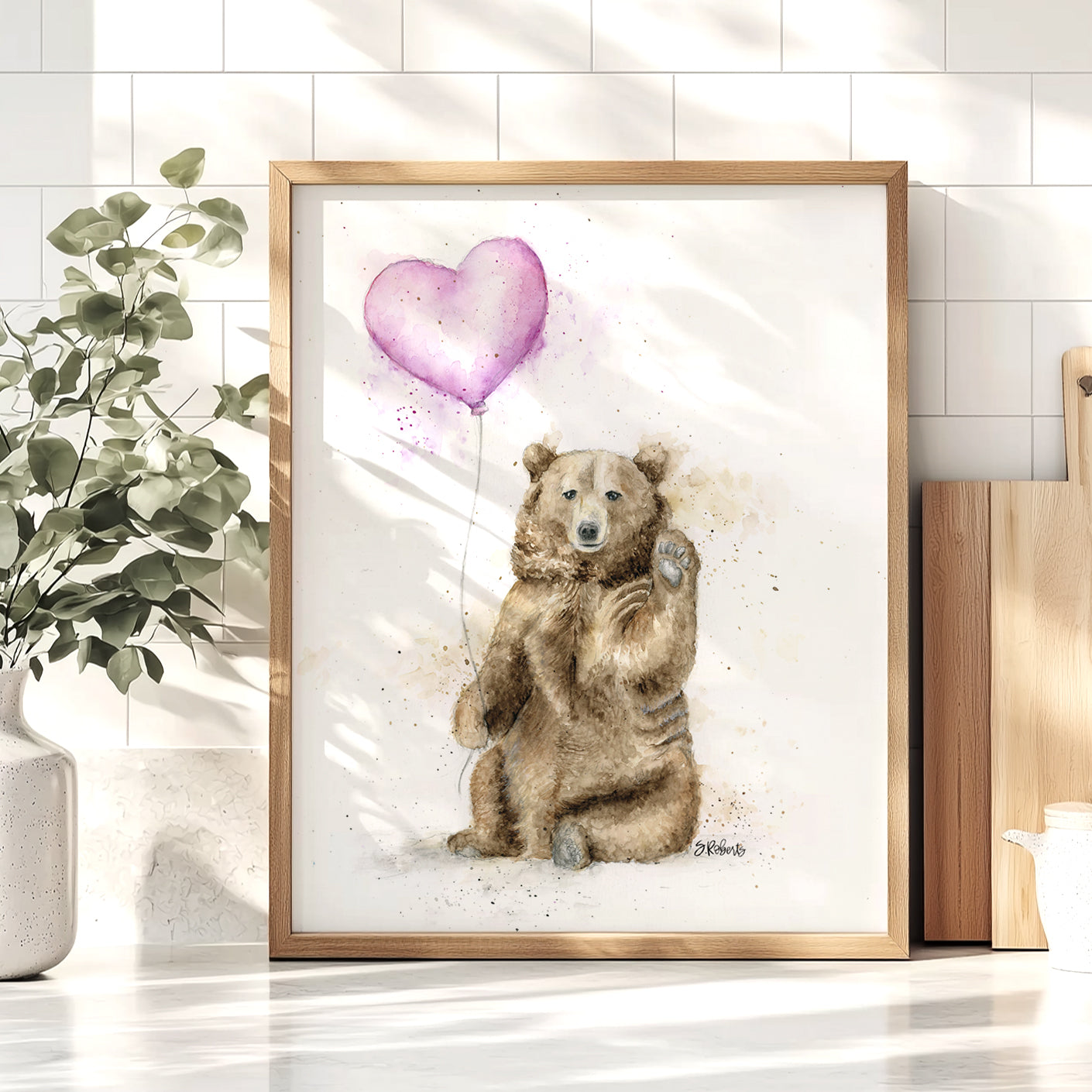 Framed artwork of a bear holding a heart-shaped balloon on a white wall.