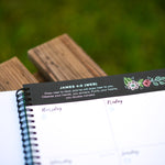 Notebook with a decorative border featuring a Bible verse scripture and illustrations on a wooden surface.