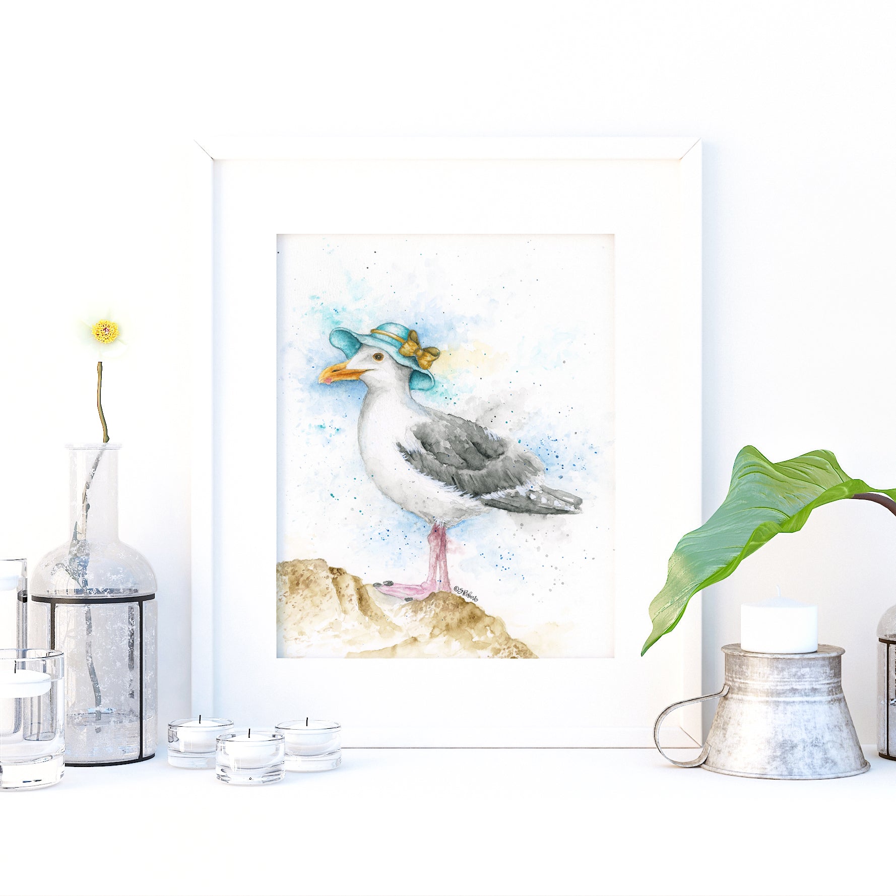 Decorative setup with a seagull painting, vase, and small plant on a white surface.